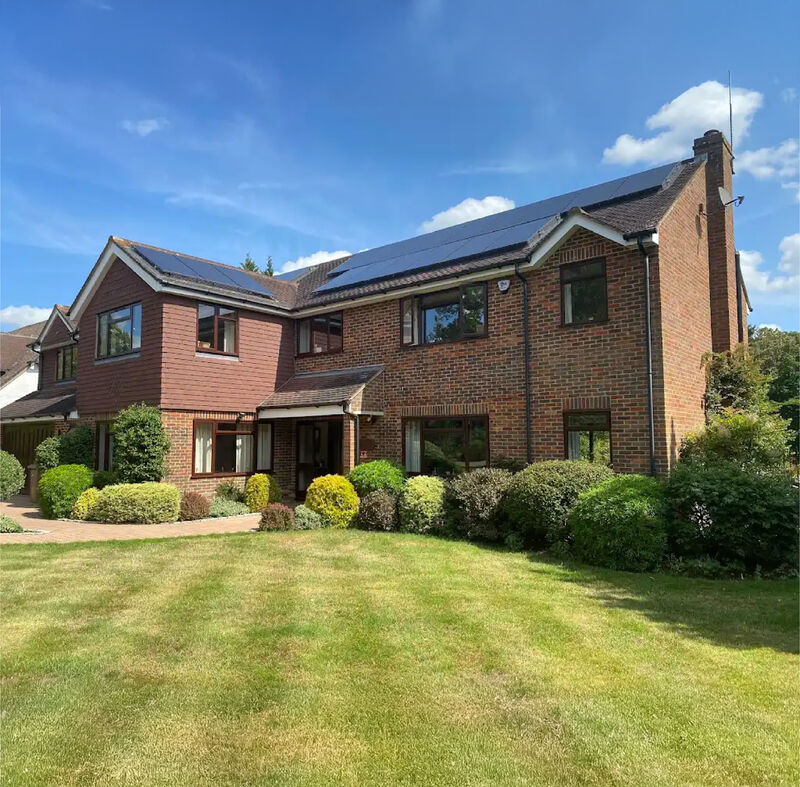A large brick house with solar panels on its roof, seen across a lawn