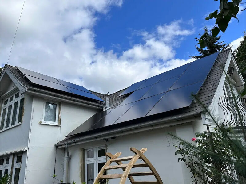 A white-rendered house with black solar panels across two slopes of its roof